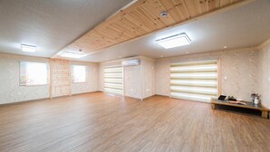 A spacious room with wooden floors, a ceiling fan, and a large window. - Jeju Ppalkanpungcha Pension (Jeju City)