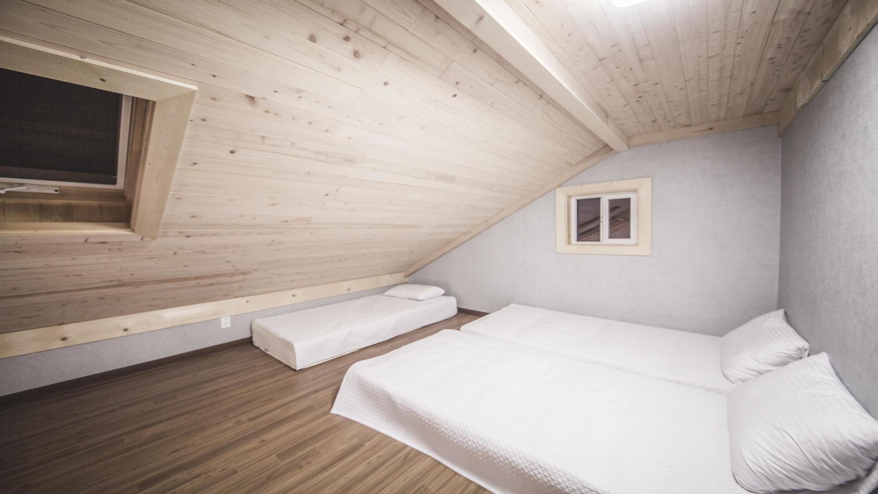 A small, sloped-roofed room with a single bed, a window, and a wooden floor.