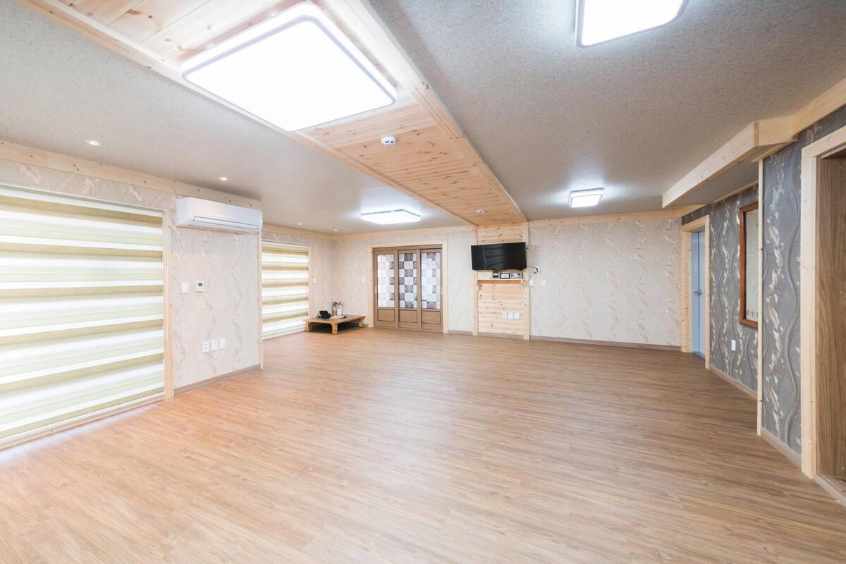 A spacious room with wooden floors, a large sliding door, and a ceiling with skylights.