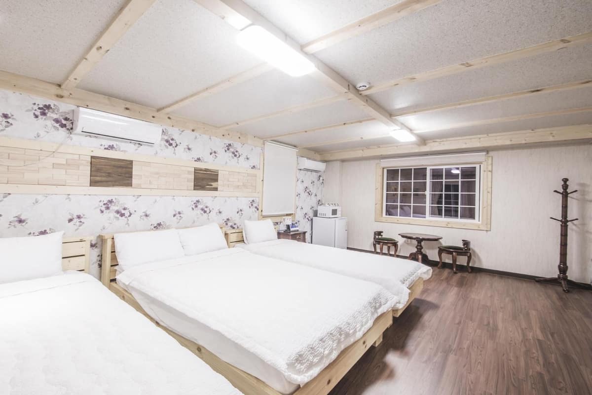 A room with three wooden beds, a window, a small table, and a coat rack.