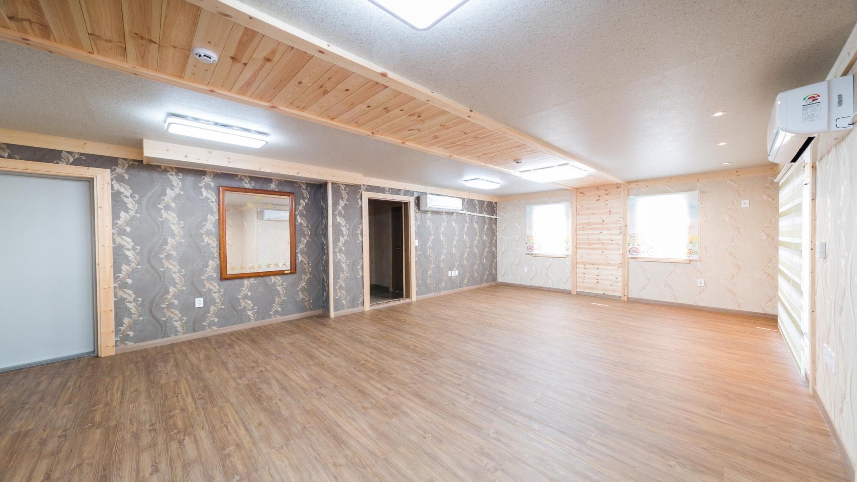 Une pièce spacieuse avec un plancher en bois, un grand miroir et une porte donnant sur une autre pièce.