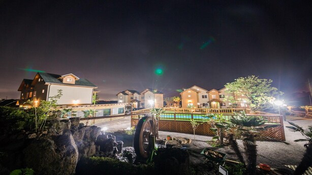 A well-lit hotel with multiple buildings, a pool area, and a bridge. - Jeju Ppalkanpungcha Pension (Jeju City)