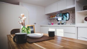 A modern kitchen with white cabinets, a wooden countertop, and a dining area with a table set for two. - Jeju Ppalkanpungcha Pension (Jeju City)