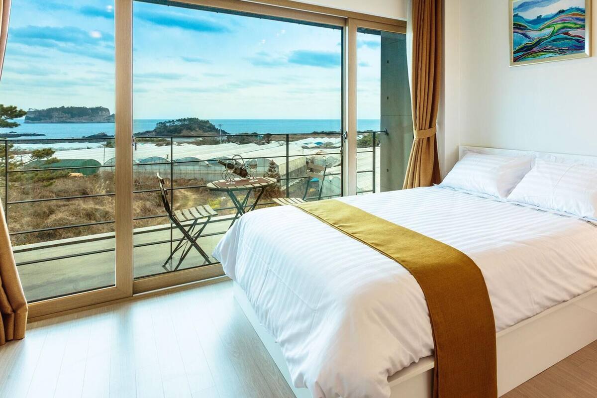 A bedroom with a large window offering a view of the sea and a distant island.