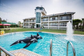 A swimming pool with inflatable orca figures, a fountain, and a multi-story building with balconies in the background. - Seogwipo Jejuhae-anhyuyang Pension (Seogwipo)