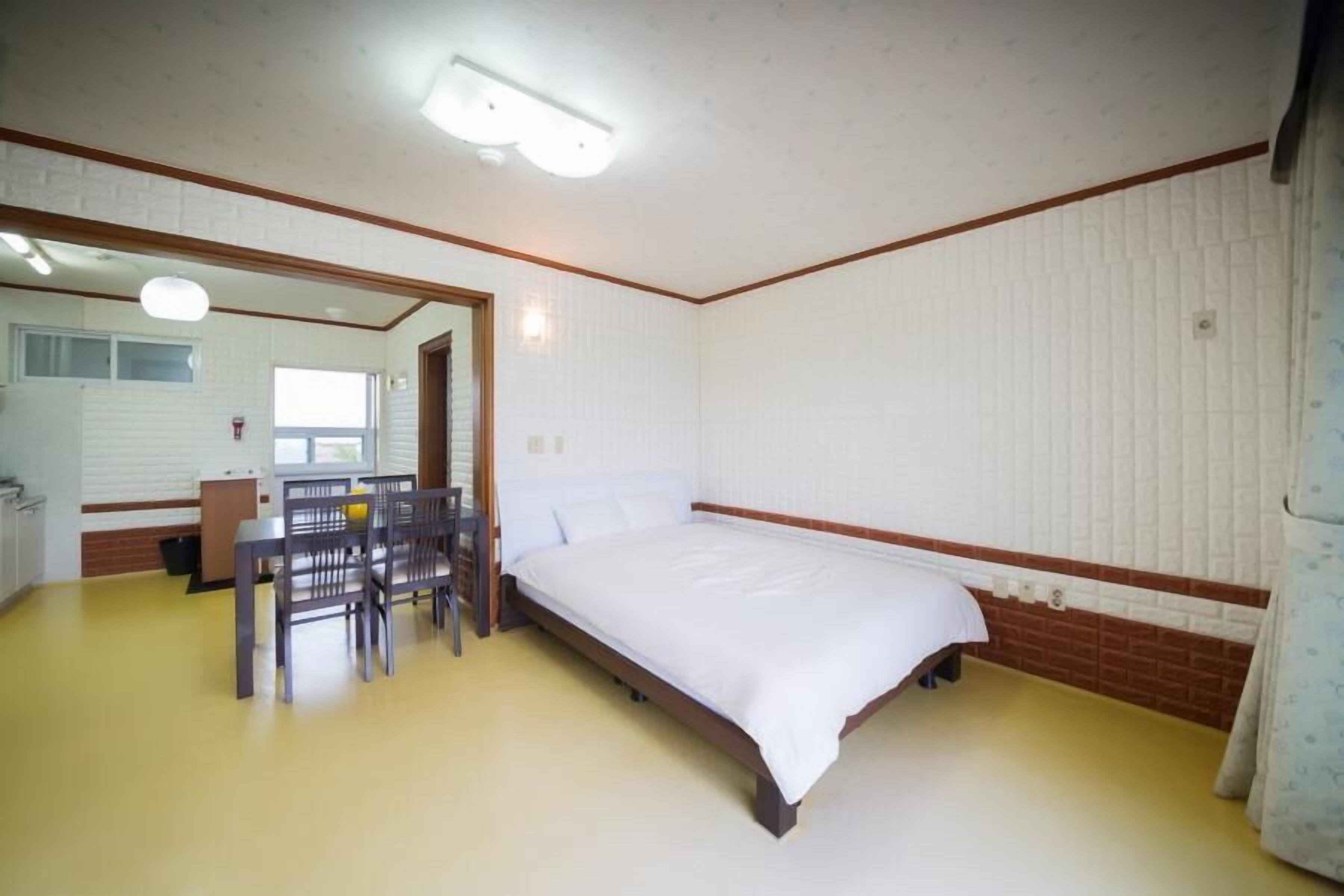 Un dormitorio con cama, escritorio y silla. Hay una ventana y una puerta.