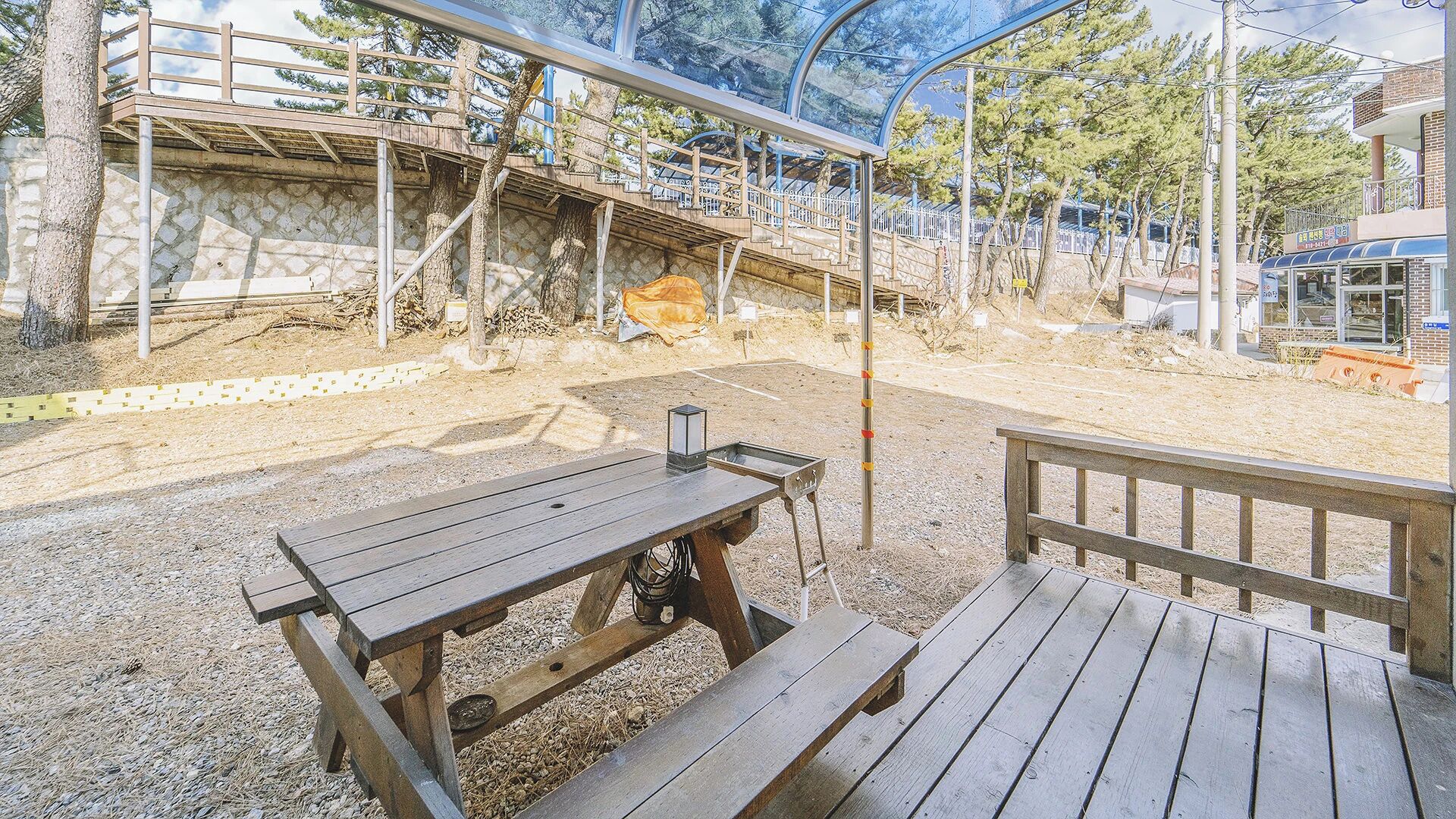 Un espacio al aire libre con bancos de madera y una mesa de picnic, rodeado por un muro de piedra y árboles.