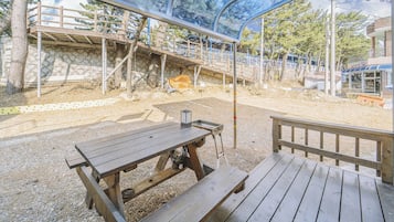 Un espacio al aire libre con bancos de madera y una mesa de picnic, rodeado por un muro de piedra y árboles.