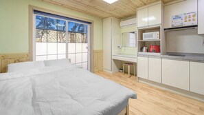 Un dormitorio con cama, ventana, kitchenette y un taburete pequeño.