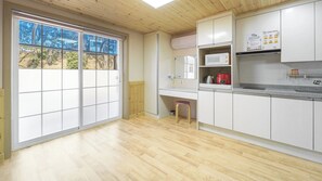 Una cocina con suelo de madera, armarios blancos, un microondas y un hervidor rojo.