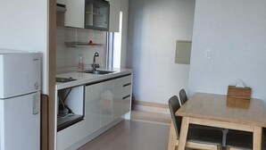 Una cocina compacta con refrigerador integrado, un lavamanos y una mesa de comedor de madera con cuatro sillas.