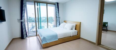 A bedroom with a bed, a TV, and a view of the outside.