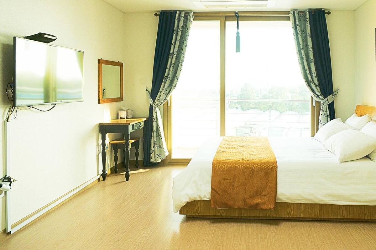 Een hotelkamer met een bed, een televisie, een bureau en een raam met gordijnen.