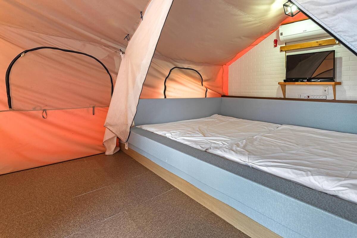 Una habitación pequeña y triangular con una cama individual, una pared de ladrillo blanco y un televisor montado.