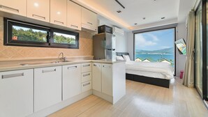 A modern kitchen with a built-in microwave, a refrigerator, and a sink. There is a bed with a view of the sea and hills. - Goseong Bluewhale Glamping (Goseong)