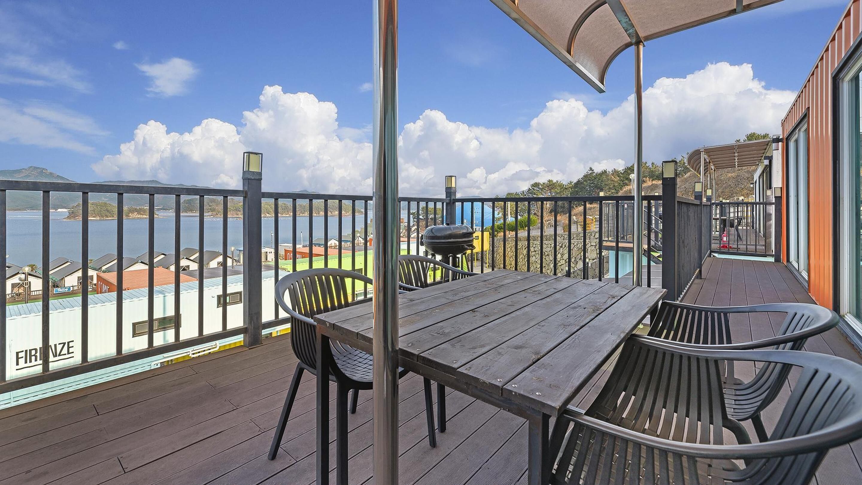 Une terrasse en bois avec une table et des chaises, d’où l’on peut admirer un plan d’eau et une île lointaine.