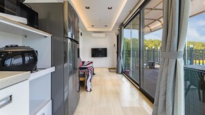 A modern kitchen with a built-in microwave, a flat-screen TV, and a sliding glass door leading to a balcony with a view of greenery. - Goseong Bluewhale Glamping (Goseong)