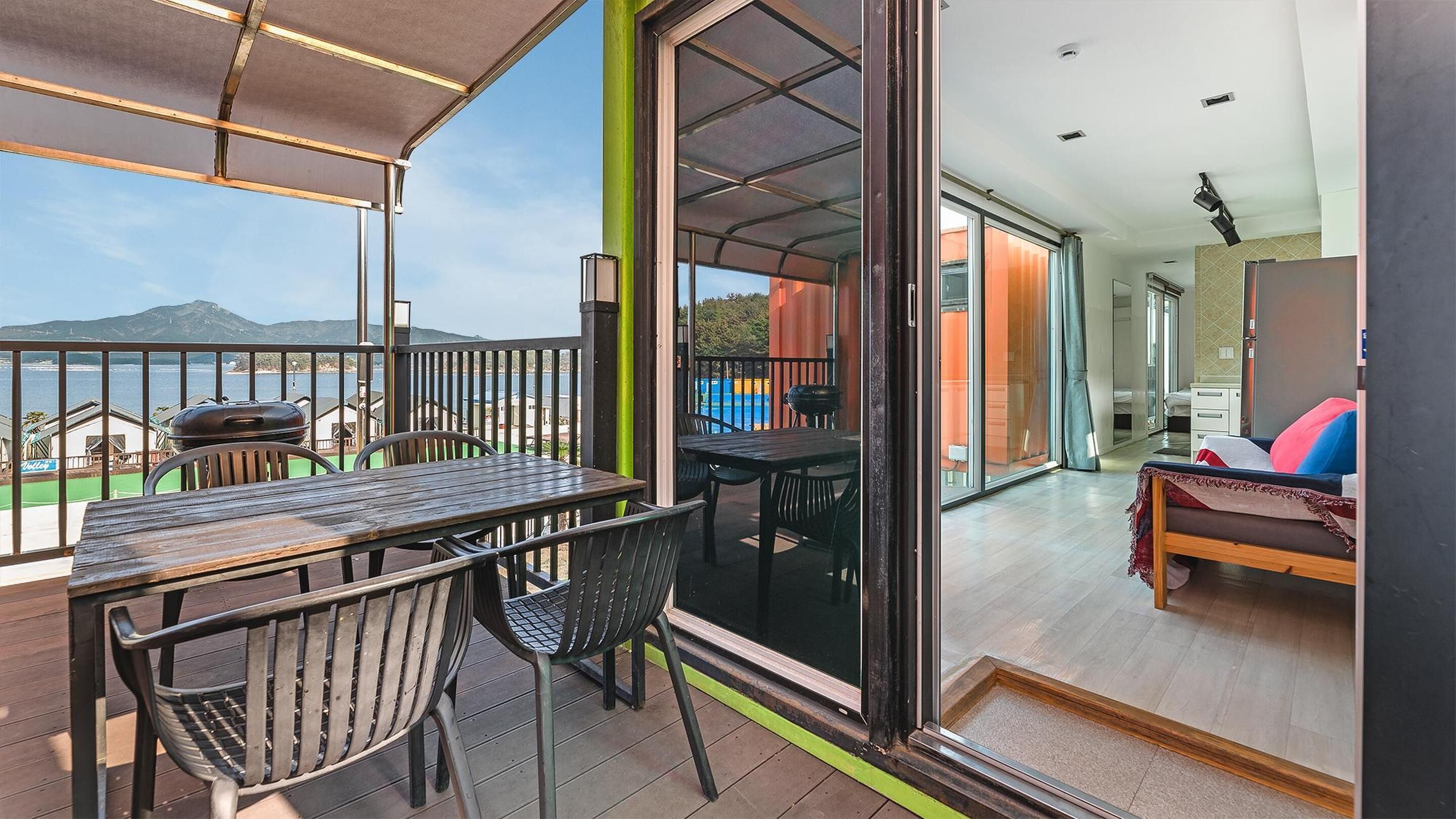 Un balcon avec une table et des chaises, une vue sur la mer et un aperçu de l’intérieur, où l’on aperçoit un lit et une salle de bain.