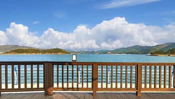 A wooden deck with a railing overlooking a calm sea and distant hills. - Goseong Bluewhale Glamping (Goseong)