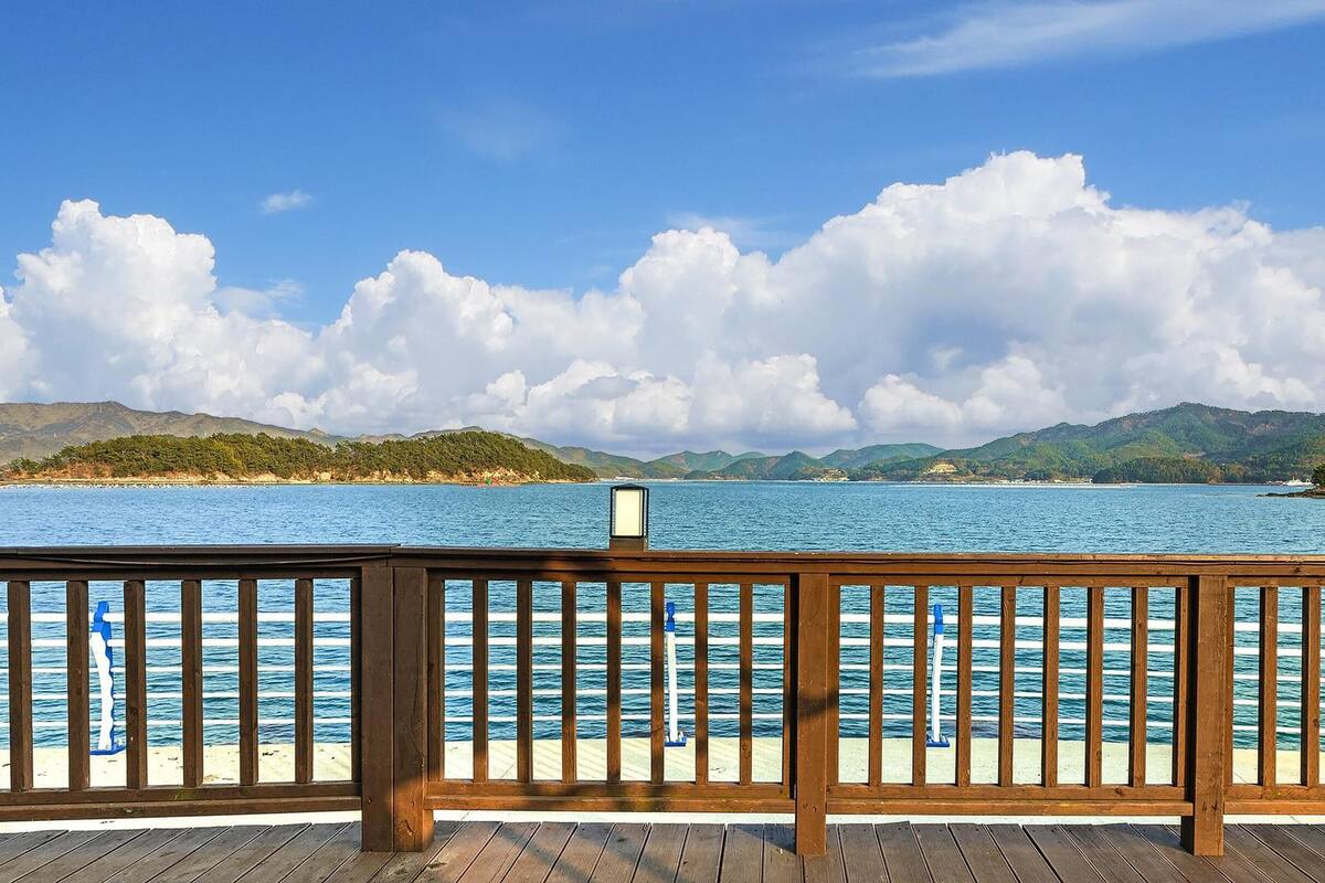Una terraza de madera con barandilla que da a un mar tranquilo y colinas lejanas.