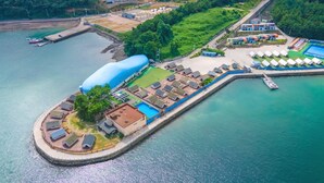 An aerial view of a coastal resort with a large blue dome structure, a marina, and a pool area. - Goseong Bluewhale Glamping (Goseong)