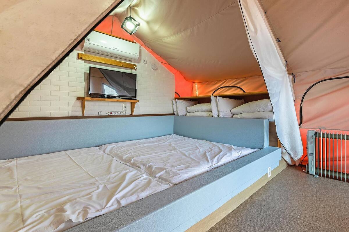 Habitación tipo tienda de campaña con una cama, un televisor y un radiador.