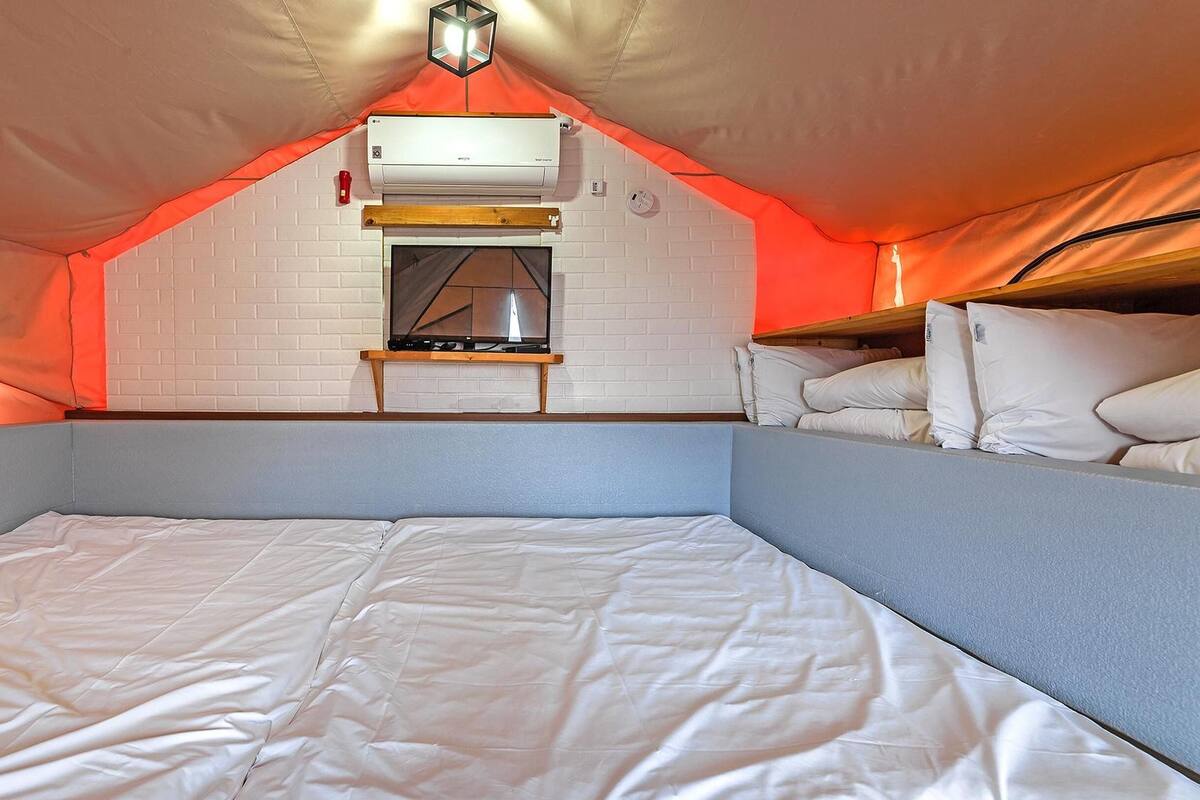 Un espacio de descanso compacto y triangular con cama, una mesita y aire acondicionado instalado.