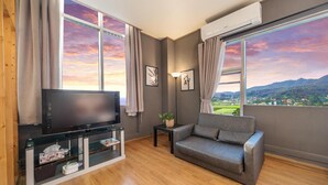 A modern living room with a flat-screen TV, a grey sofa, and a small table with a plant. Large windows offer a view of a mountainous landscape. - Ganghwa Chocolate Pension (Incheon)