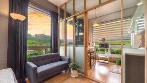 A modern room with a grey sofa, a small table with a plant, and a view of a green landscape through large windows. - Ganghwa Chocolate Pension (Incheon)