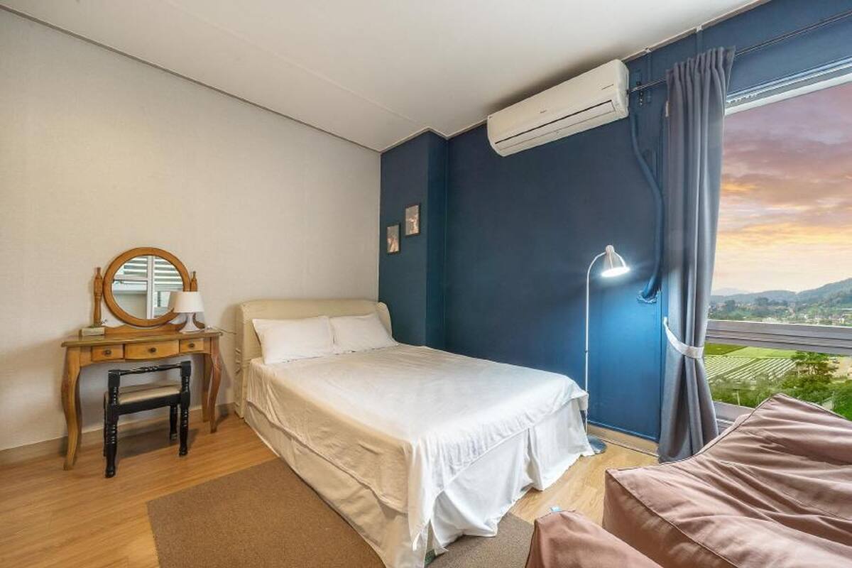 Een slaapkamer met een bed, een bureau met spiegel, een lamp en uitzicht op het landschap.