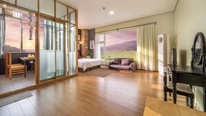 A modern hotel room with a large bed, a sofa, a dining table, and a view of the mountains. - Ganghwa Chocolate Pension (Incheon)