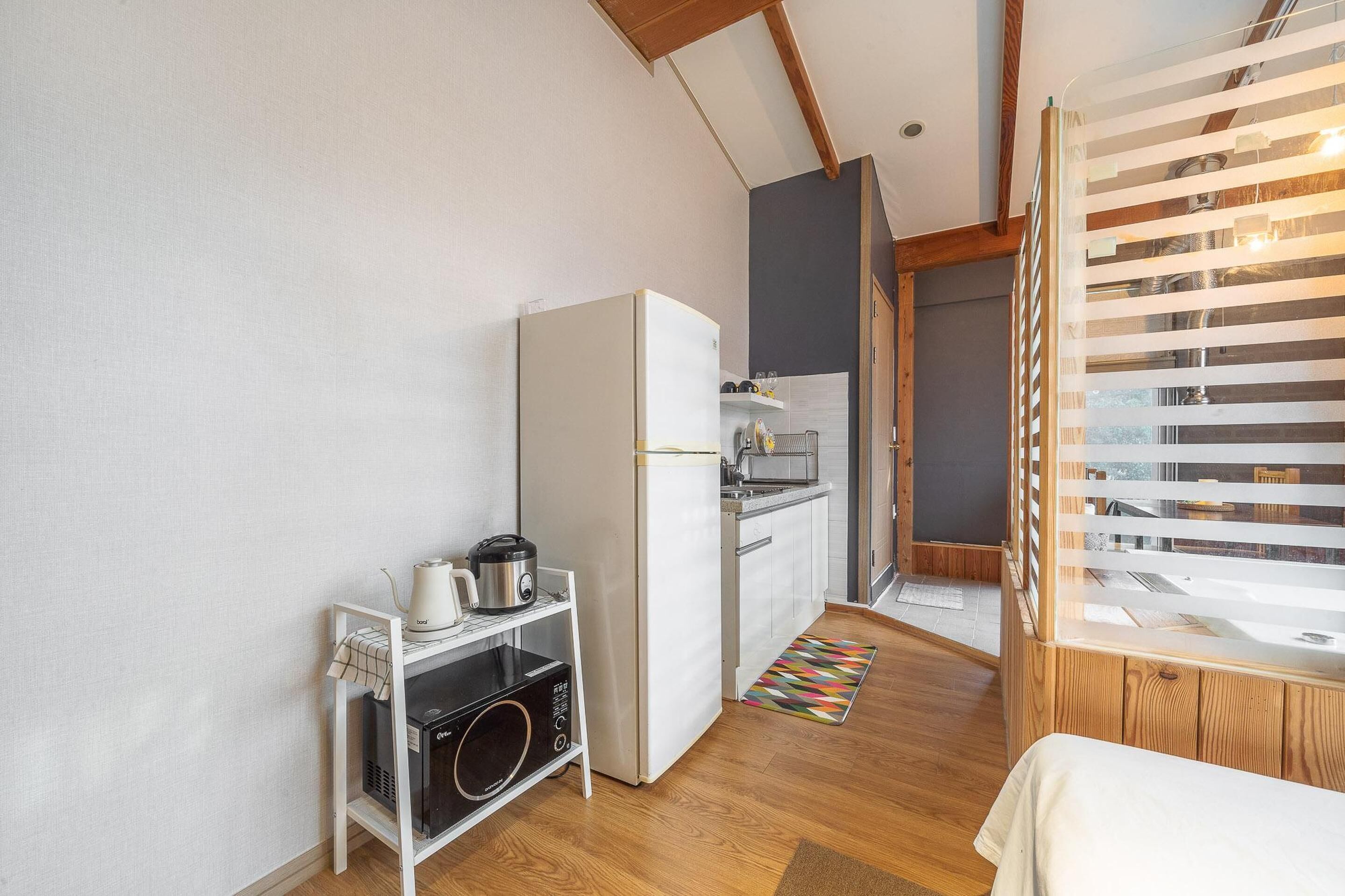 Cozinha compacta com geladeira, micro-ondas e chaleira em bancada branca.
