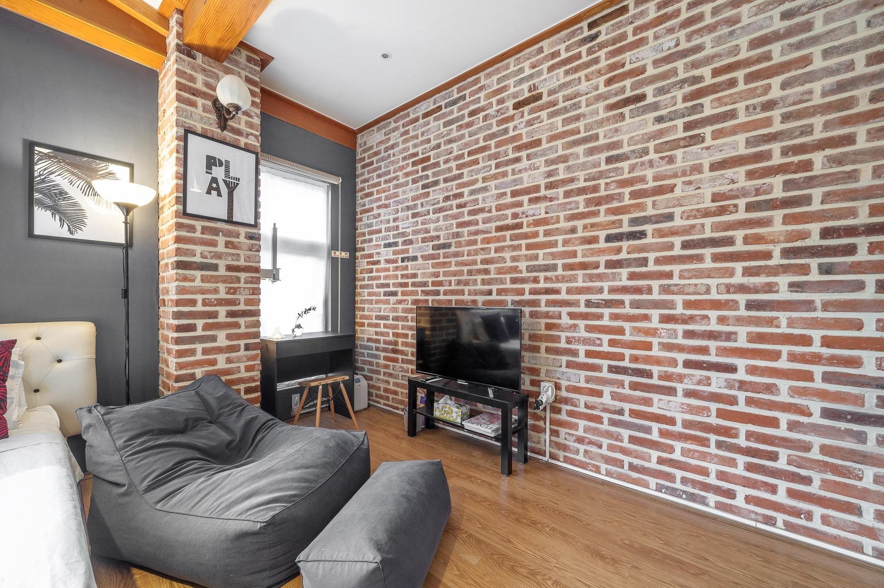 Una sala de estar con pared de ladrillo, televisor de pantalla plana, sofá y lámpara.