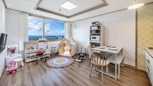 Une salle de jeux pour enfants avec une grande fenêtre, une maisonnette, une coiffeuse avec un miroir et une petite table à manger.