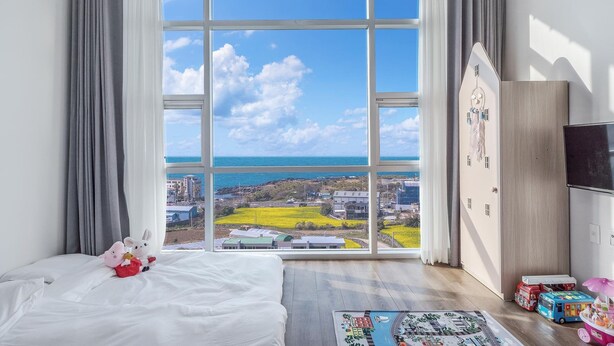 Une chambre avec une grande fenêtre, un lit, une commode et un téléviseur.