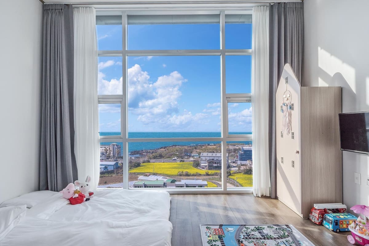 Un dormitorio con un ventanal grande, una cama, un tocador y un televisor.