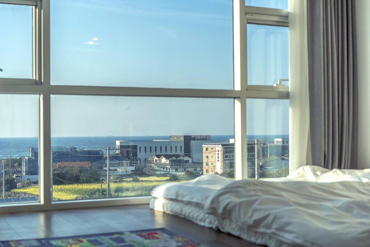 Un dormitorio con un ventanal que ofrece vistas al mar y edificios.