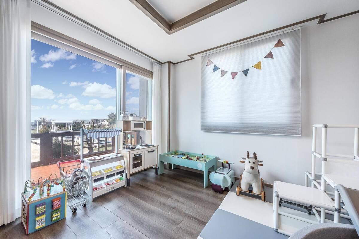 Una habitación luminosa con un ventanal grande, una zona de juegos con juguetes y vistas al exterior.