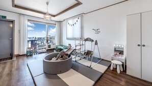 Une chambre moderne dotée d’une grande fenêtre, d’un espace de jeux, d’une coiffeuse avec un miroir et d’une armoire.