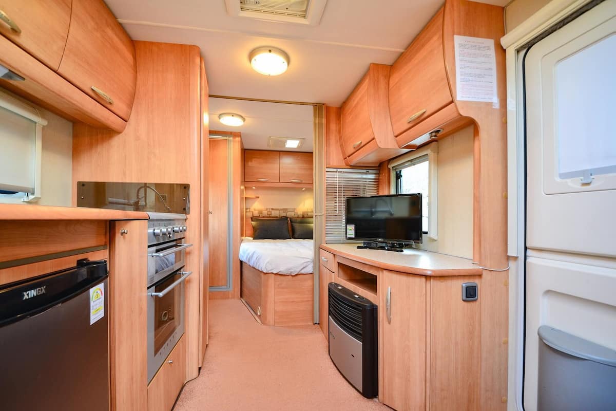 A compact kitchen with wooden cabinets, a stove, a refrigerator, and a television.