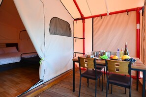 Alojamiento con carpa que incluye una cama, una mesa con comida y bebidas, y sillas.