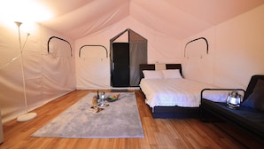 A tented room with a bed, a chair, a table with a lamp, and a small table with a bottle and a bowl of fruit. - Gwangneung Haeoreum Camping&glamping (Pocheon)