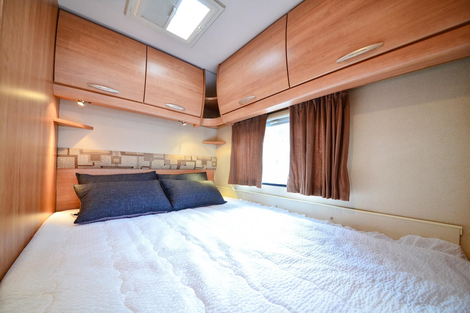 A bedroom with a bed, wooden cabinets, a window with curtains, and a skylight.