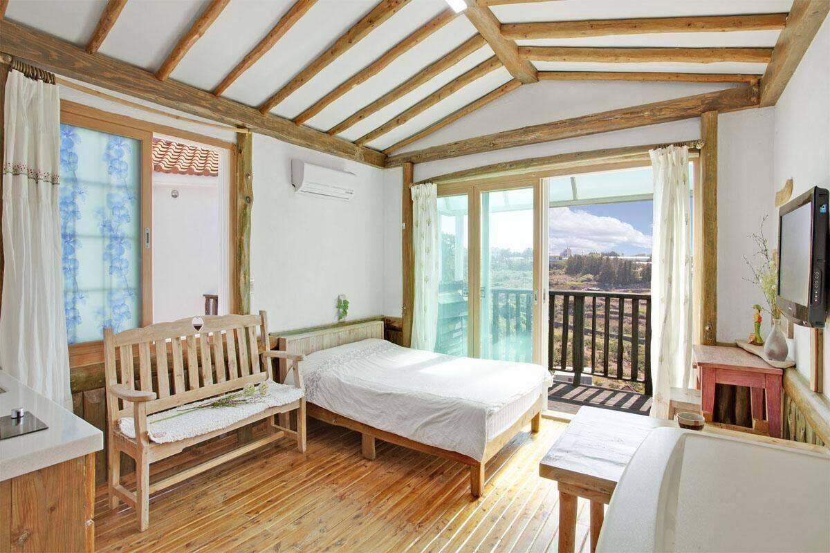 Une chambre avec un lit, un banc en bois et un balcon offrant une vue.