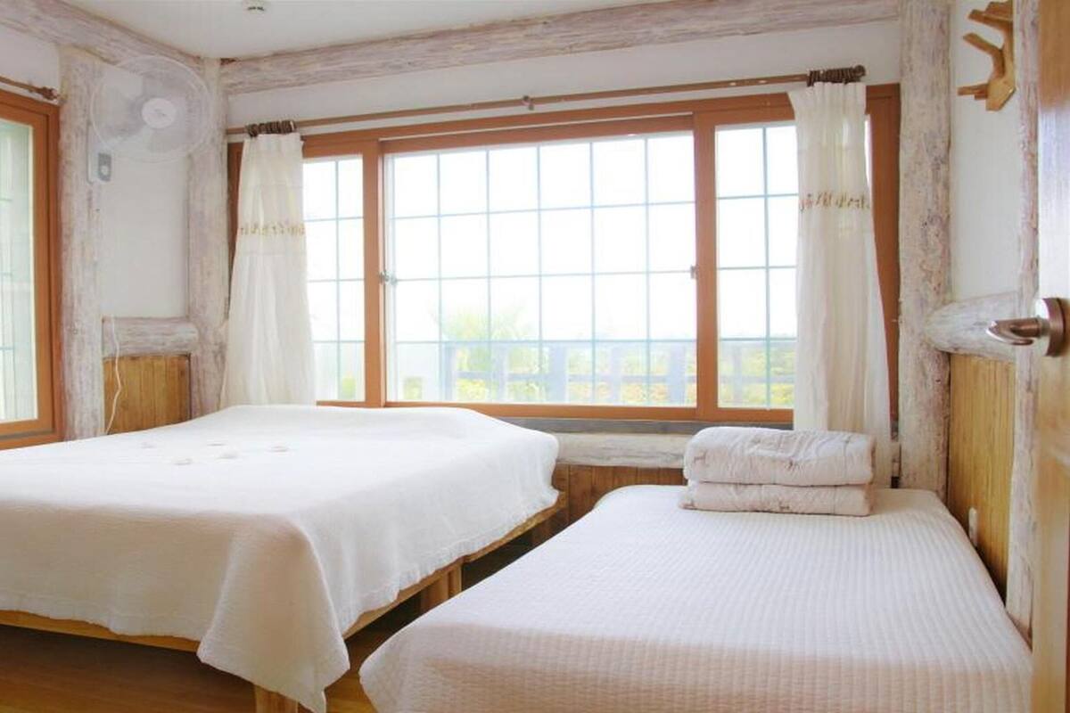 Une chambre avec deux lits, de grandes fenêtres et un banc en bois.