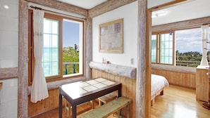 A room with wooden walls, a wooden bed, a table with benches, and large windows offering a view of greenery. - Jeju Beautiful Resort (Seogwipo)