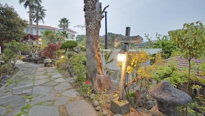 A garden pathway with stone tiles leading to a wooden signpost with directional arrows. - Jeju Beautiful Resort (Seogwipo)
