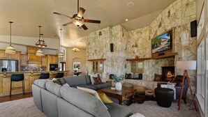 A spacious living area with a stone wall, a fireplace, a large sectional sofa, and a kitchen in the background. - Paradise by the lake - Lonestar Lakehouse (Temple)