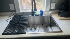 Una cocina con un lavamanos de acero inoxidable, un escurreplatos y una ventana con vistas a una terraza de madera.