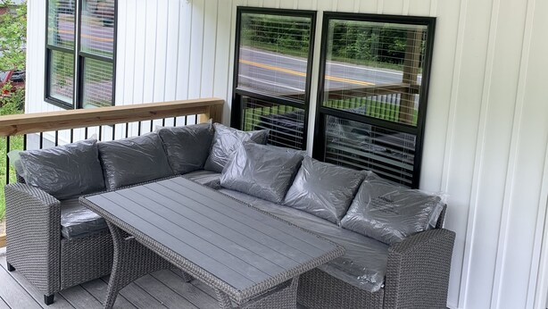 Un espacio de estar techado al aire libre con mesa y mobiliario de mimbre, ventanas amplias y ventilador de techo.
